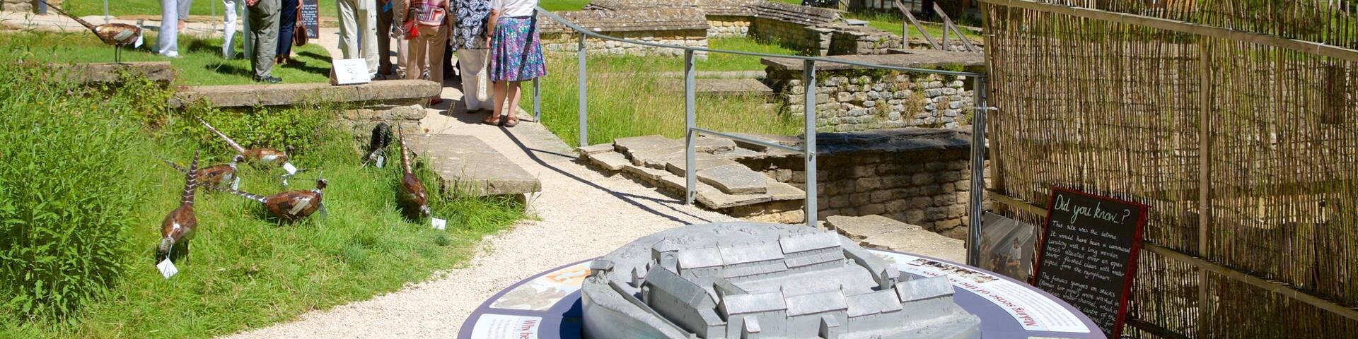 A historical site with a model of a water wheel, a wooden house, and a group of people observing the exhibits.
