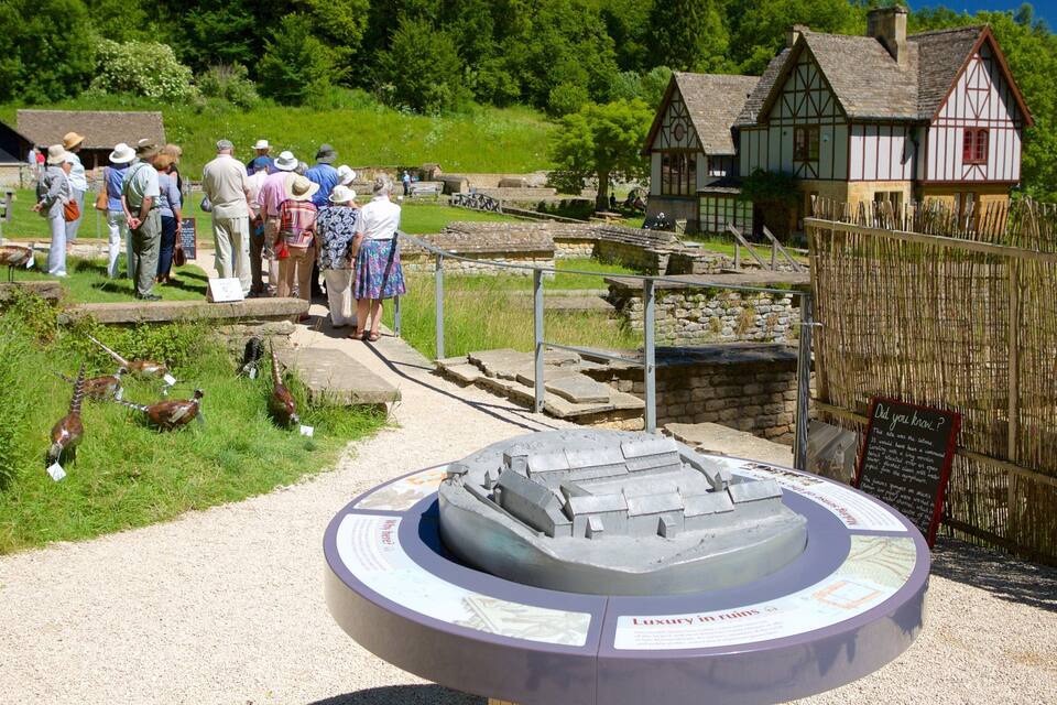 A historical site with a model of a water wheel, a wooden house, and a group of people observing the exhibits.