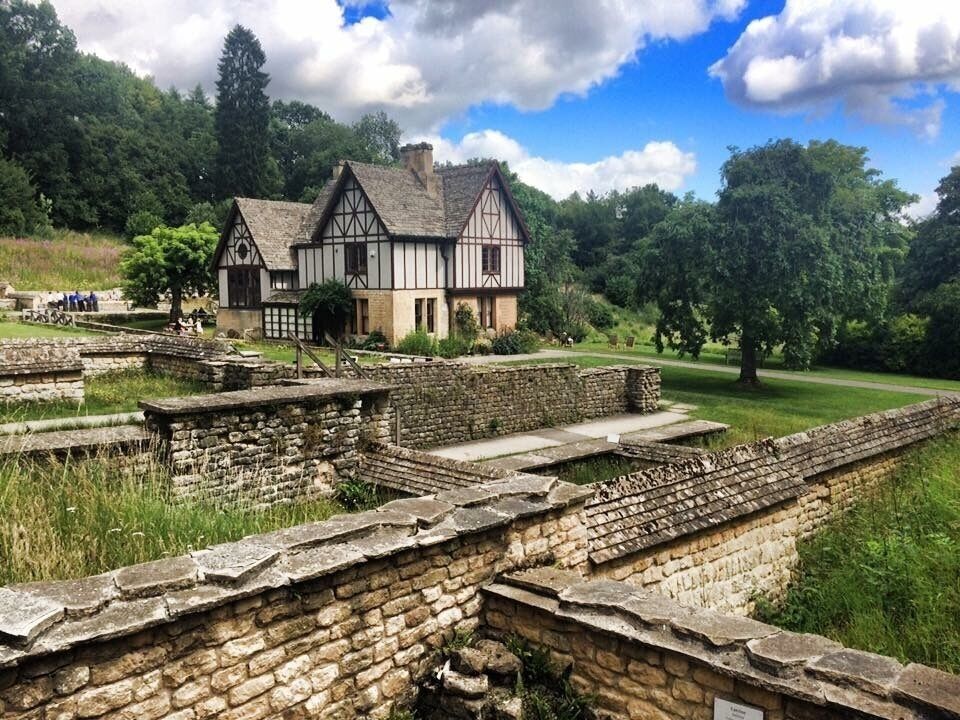 Ancient stone ruins with a Tudor-style house in the background.