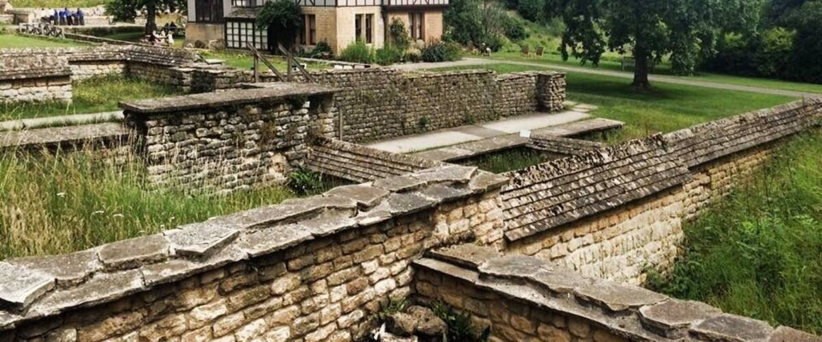 Ancient stone ruins with a Tudor-style house in the background.