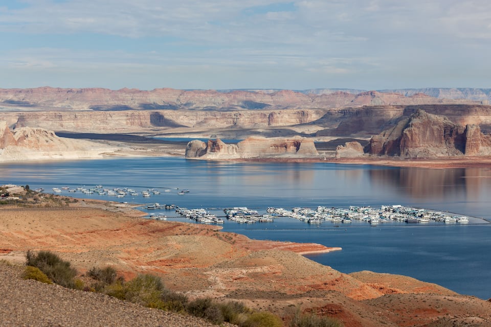 A large body of water with boats, a marina, and a desert landscape with red and brown terrain.