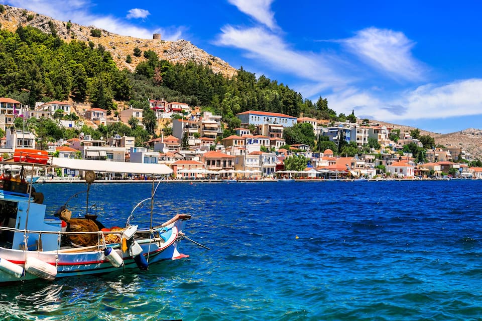 A coastal town with houses on a hillside, a boat docked at the pier, and a clear blue sea.