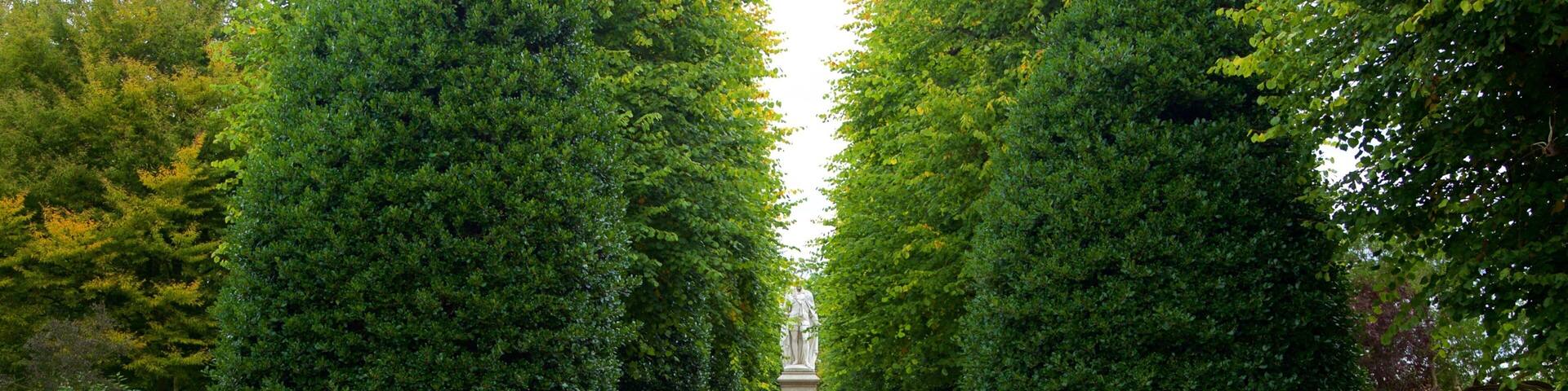 A formal garden with a central statue, surrounded by neatly trimmed hedges and vibrant flower beds.