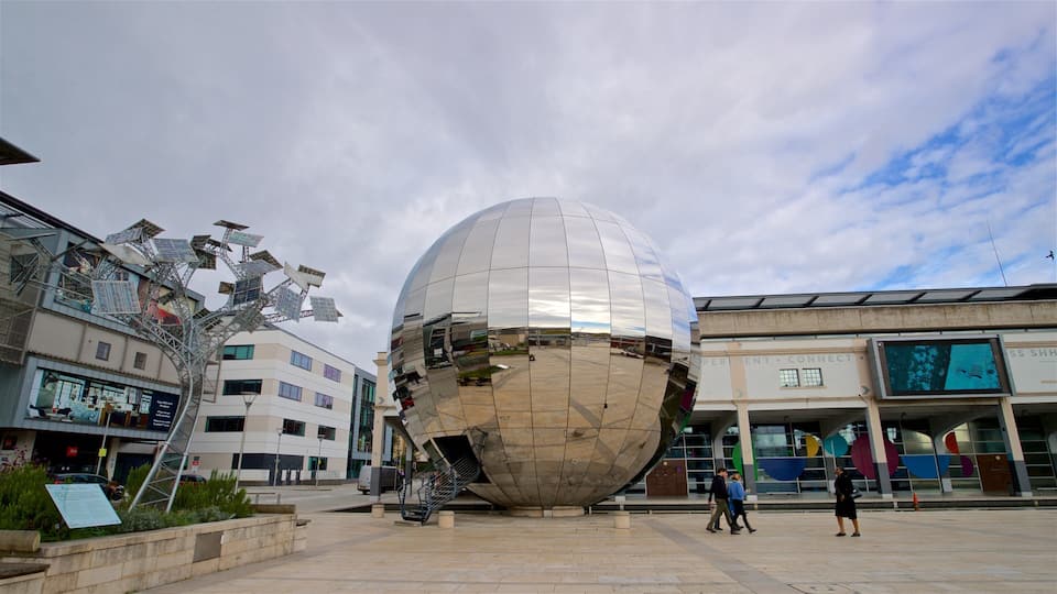 Una esfera reflectante de gran tamaño en una plaza urbana, con edificios circundantes y cielo despejado.