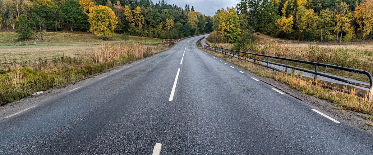 A two-lane road curving through a forested area with autumn-colored trees.
