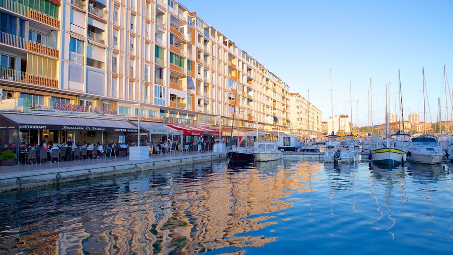 A marina with boats docked, a waterfront restaurant, and a multi-story building with balconies.