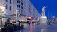 Eine Uferpromenade mit einer Statue, Cafés und einer Reihe von Hotels.