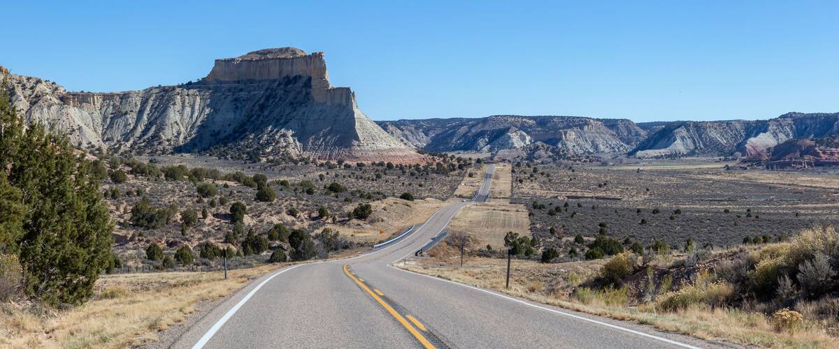 A winding road through a desert landscape with prominent rock formations and sparse vegetation.