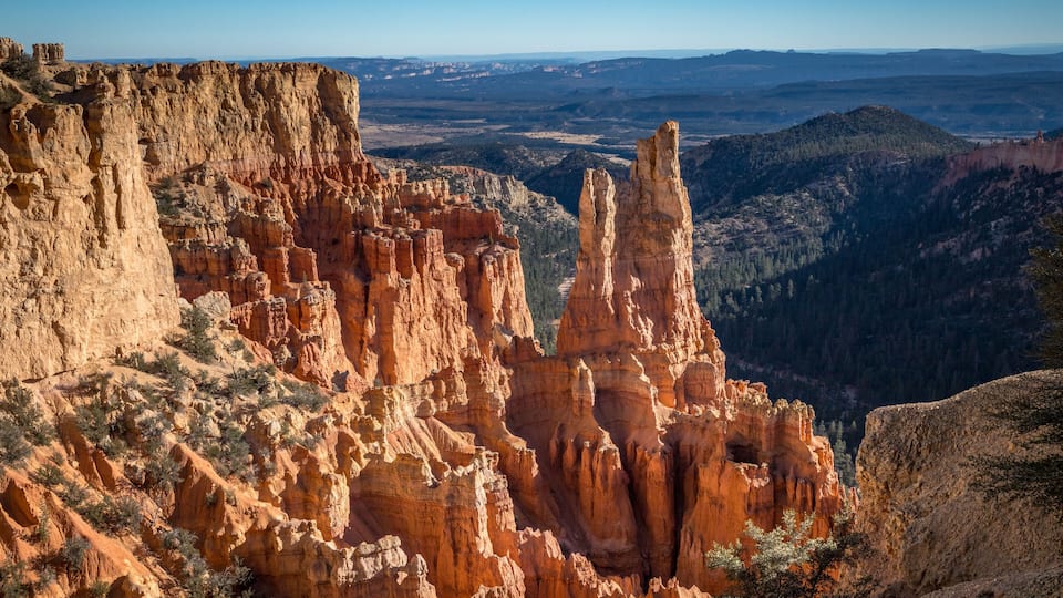 A canyon with prominent red rock formations and a distant view of a valley.
