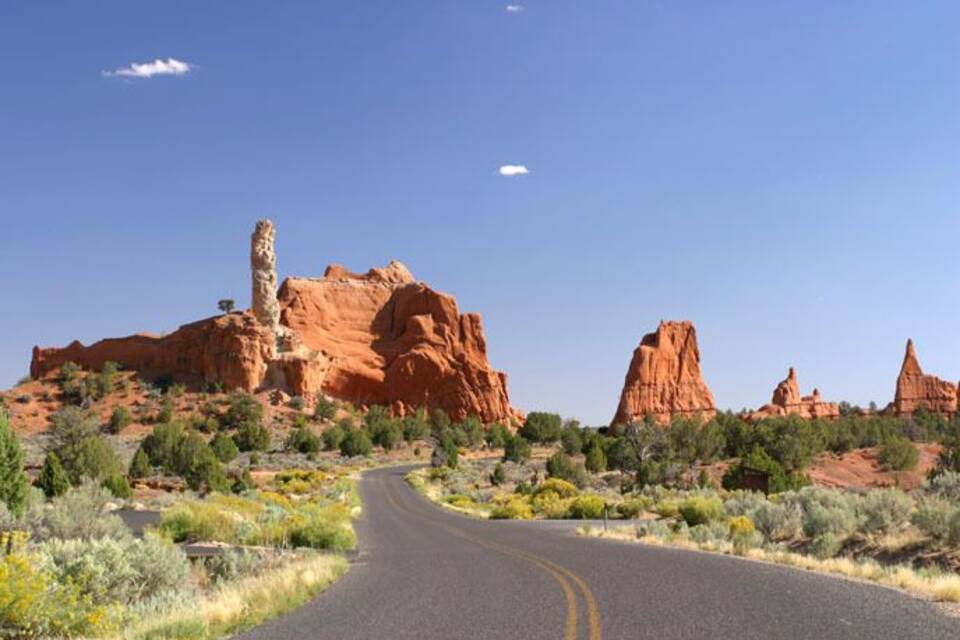 A winding road through a desert landscape with red rock formations and sparse vegetation.