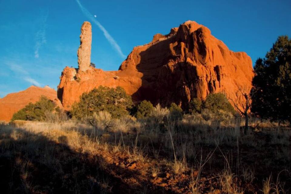 A large red rock formation with a prominent vertical pillar in a desert landscape.