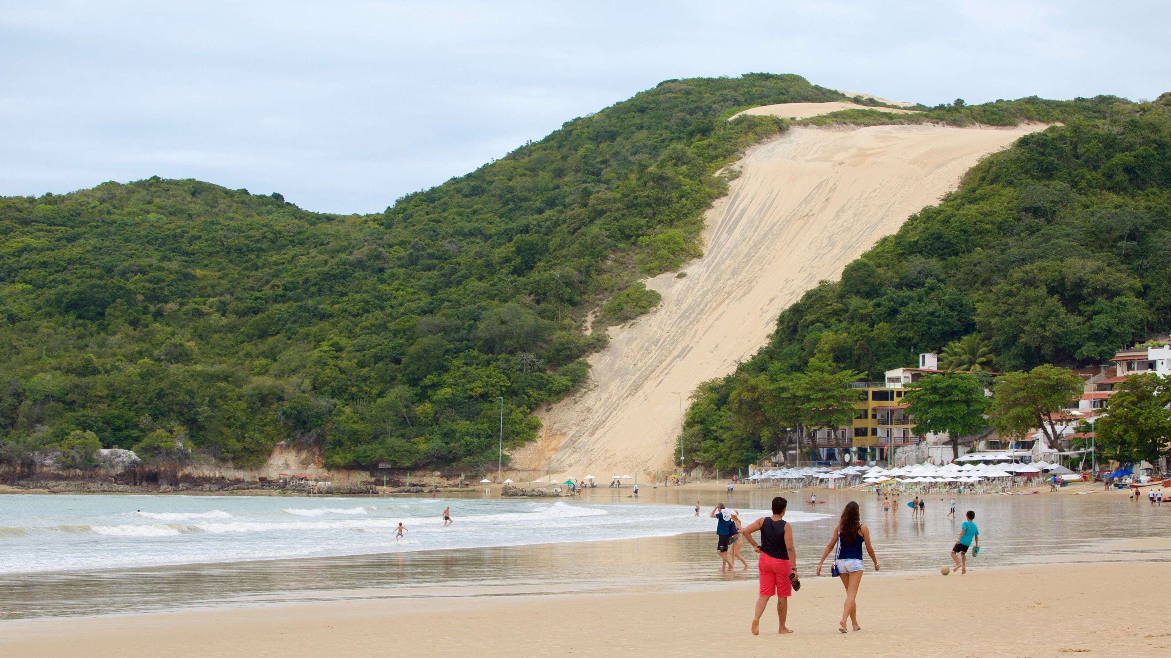 A beach with a steep, sandy slope leading to the ocean, surrounded by lush green hills.