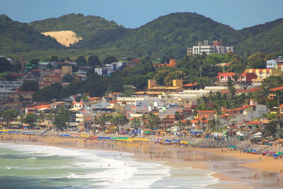 A coastal town with a beach, buildings, and hills in the background.