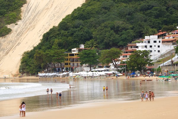 Une plage avec une falaise abrupte, des parasols et des bâtiments.