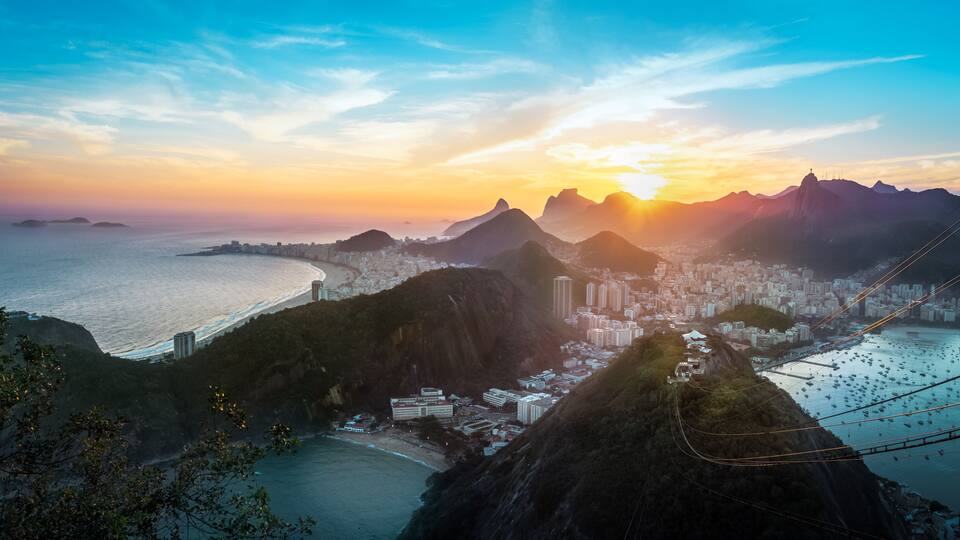 Uma cidade costeira com uma cadeia de montanhas imponente, uma praia e um sistema de teleférico.