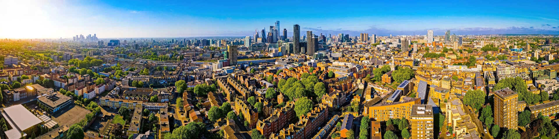 A panoramic view of a city with dense urban architecture, green spaces, and a clear blue sky.