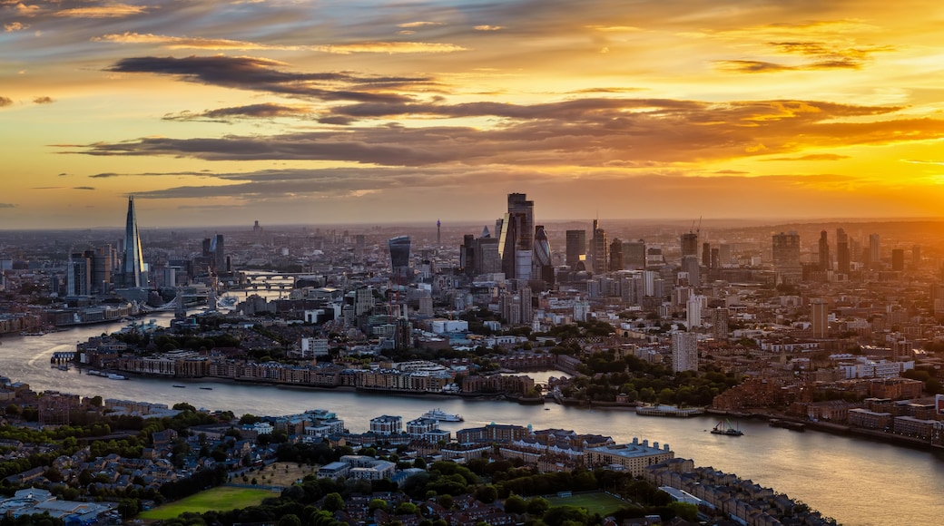 Une vue sur une ville au coucher du soleil, avec une rivière qui la traverse, mettant en valeur des gratte-ciel modernes et des bâtiments historiques.