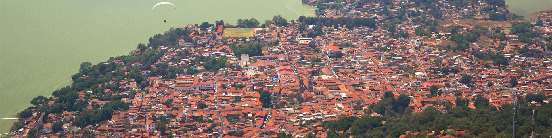 Un pueblo costero con edificios de techo rojo, un lago verde y montañas al fondo.