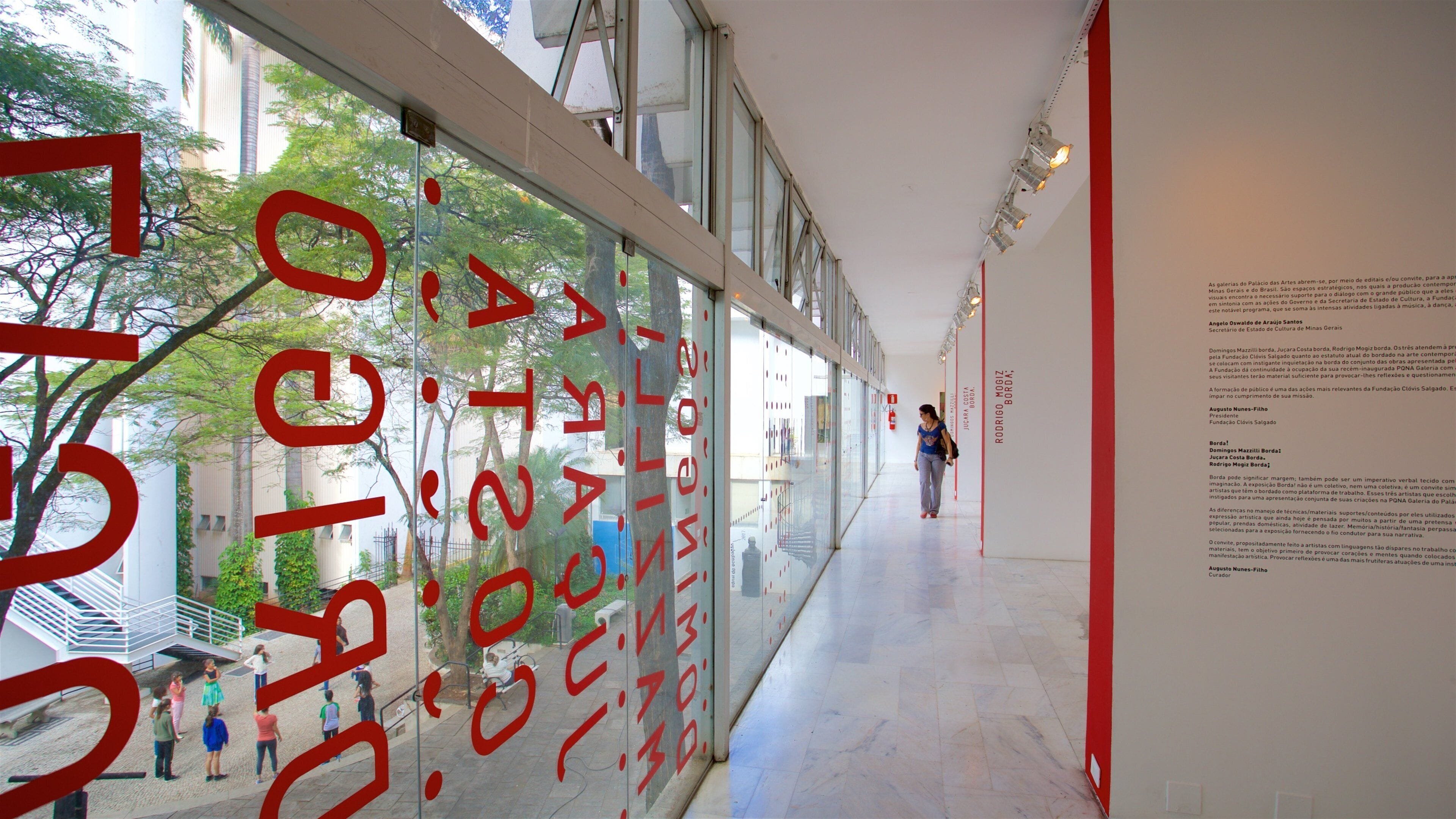 Un couloir avec de grandes lettres rouges sur le mur de verre, une personne qui marche et un escalier sur la gauche.
