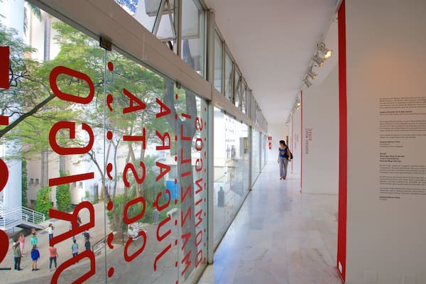 A corridor with large red letters on the glass wall, a person walking, and a staircase on the left.