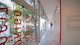 Un couloir avec de grandes lettres rouges sur le mur de verre, une personne qui marche et un escalier sur la gauche.