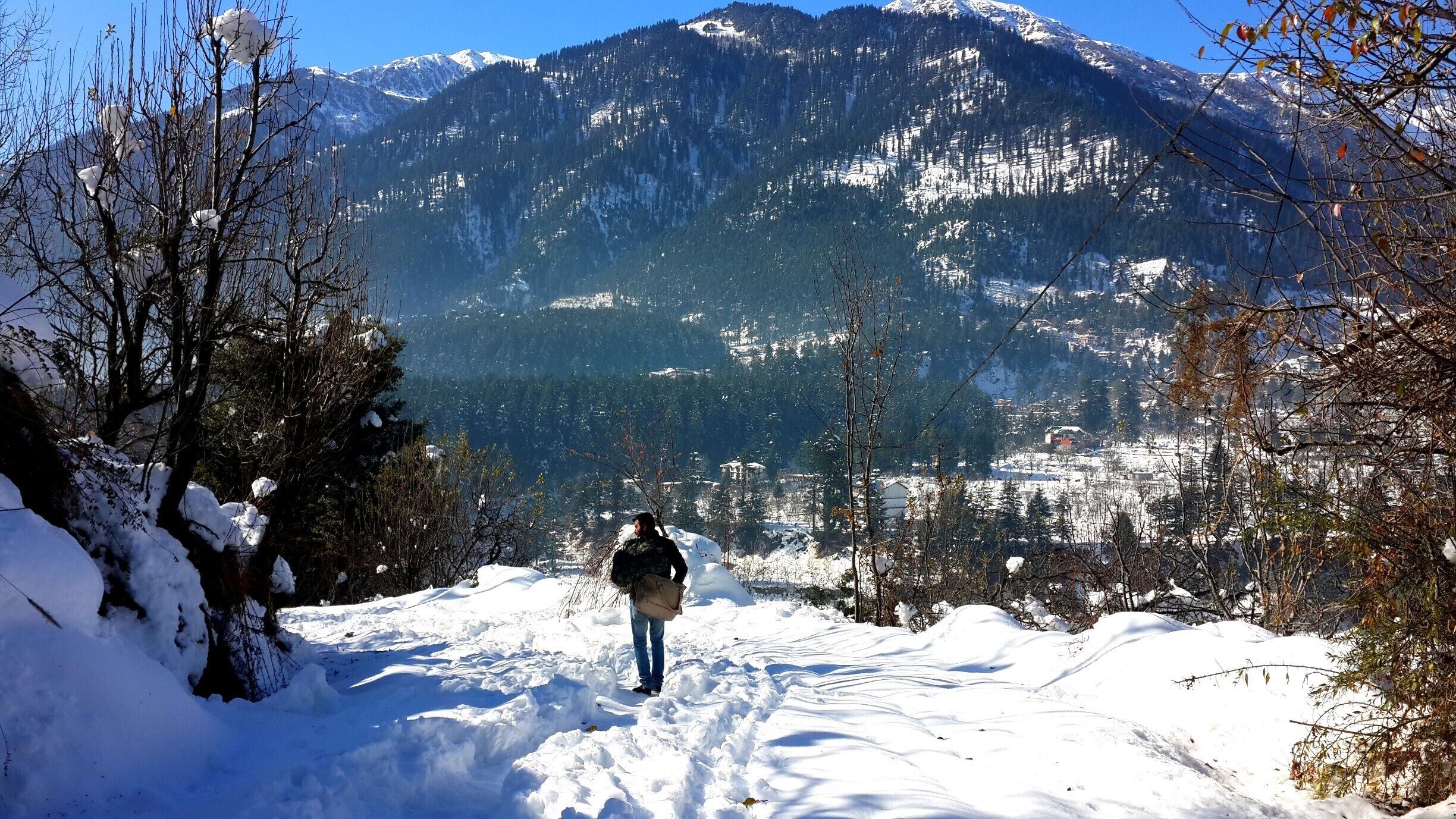 A person walking on a snow-covered path with mountains in the background.