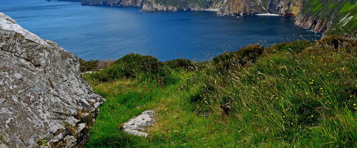 A coastal landscape with cliffs, a body of water, and grassy terrain.