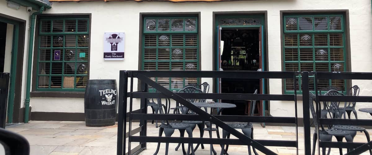The Rusty Mackerel pub with a signboard, multiple windows, and outdoor seating.