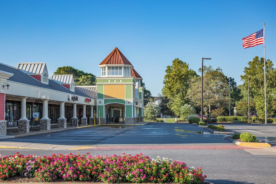 A shopping plaza with a green and white building, a red-roofed tower, and an American flag.
