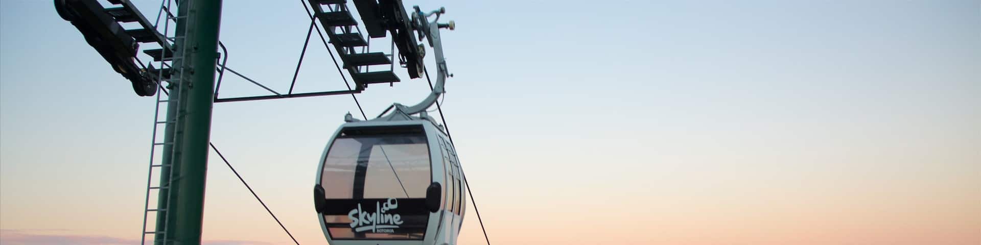 A cable car with 'Skyline' written on it, flying over a town with a lake and hills in the background.