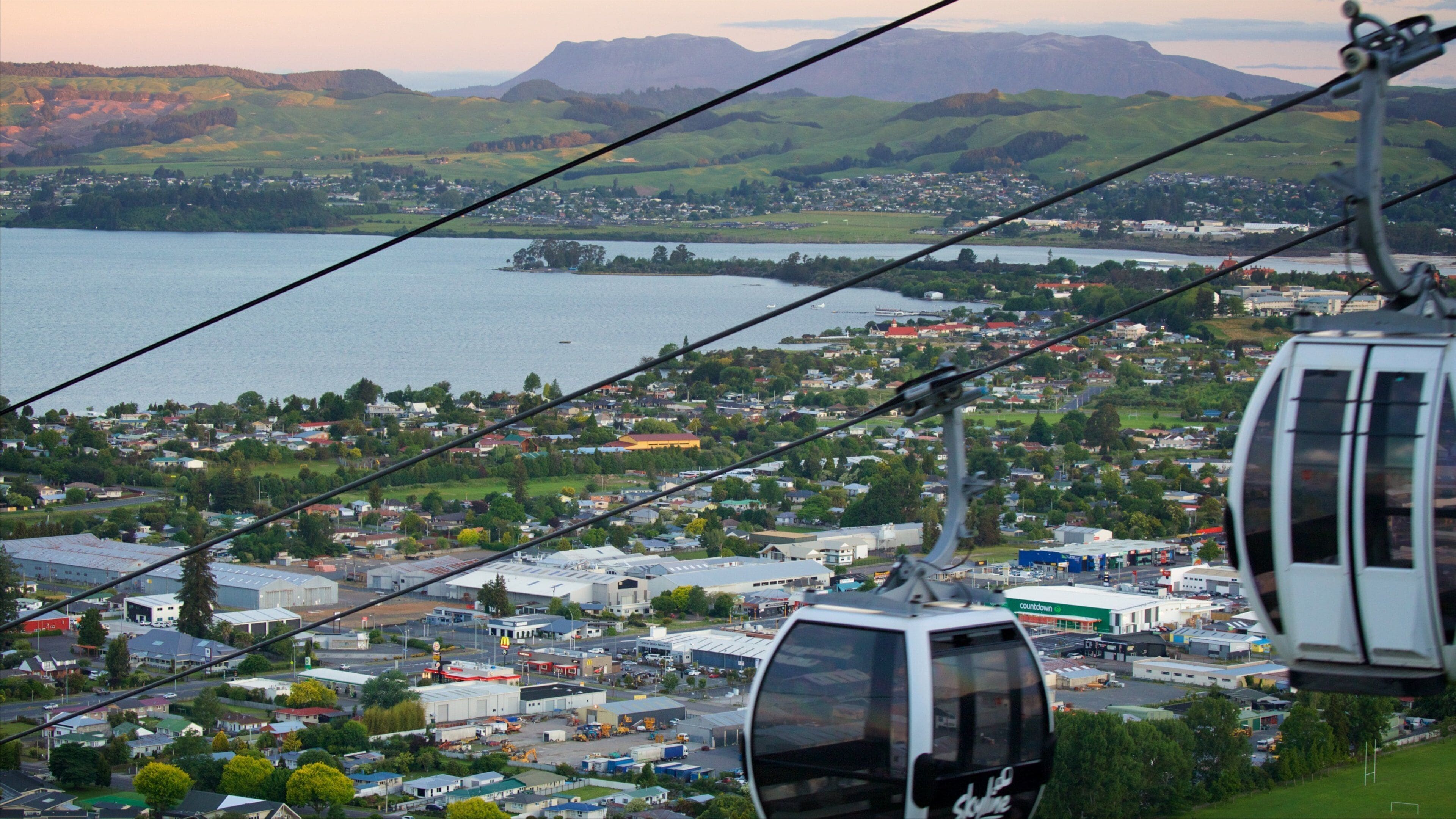 Um teleférico sobre uma cidade, com um lago e montanhas ao fundo.