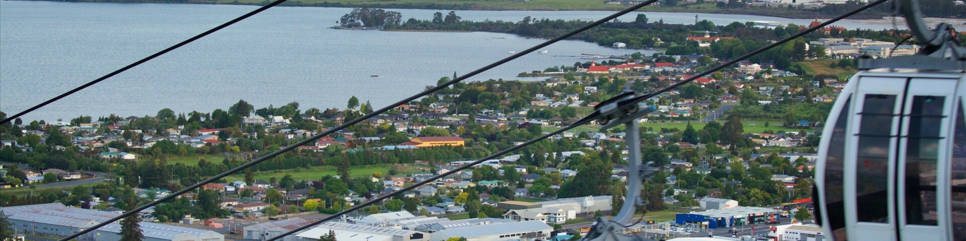 Um teleférico sobre uma cidade, com um lago e montanhas ao fundo.
