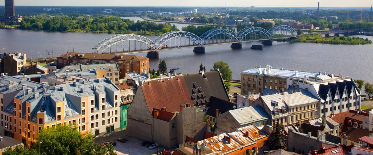 A river with a steel bridge, surrounded by buildings and greenery.