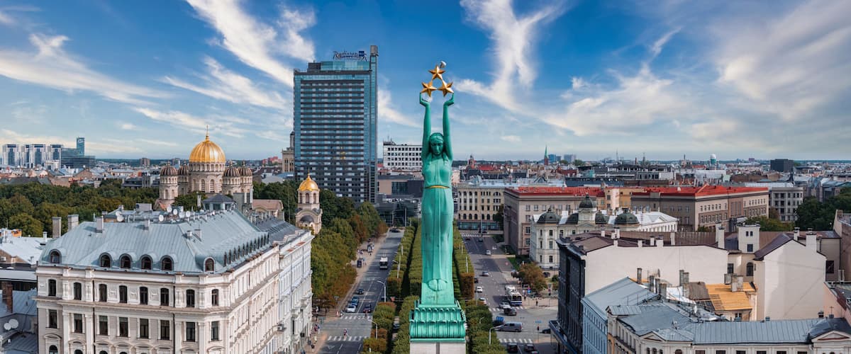 A cityscape with a prominent green statue, historic buildings, and a modern skyscraper.