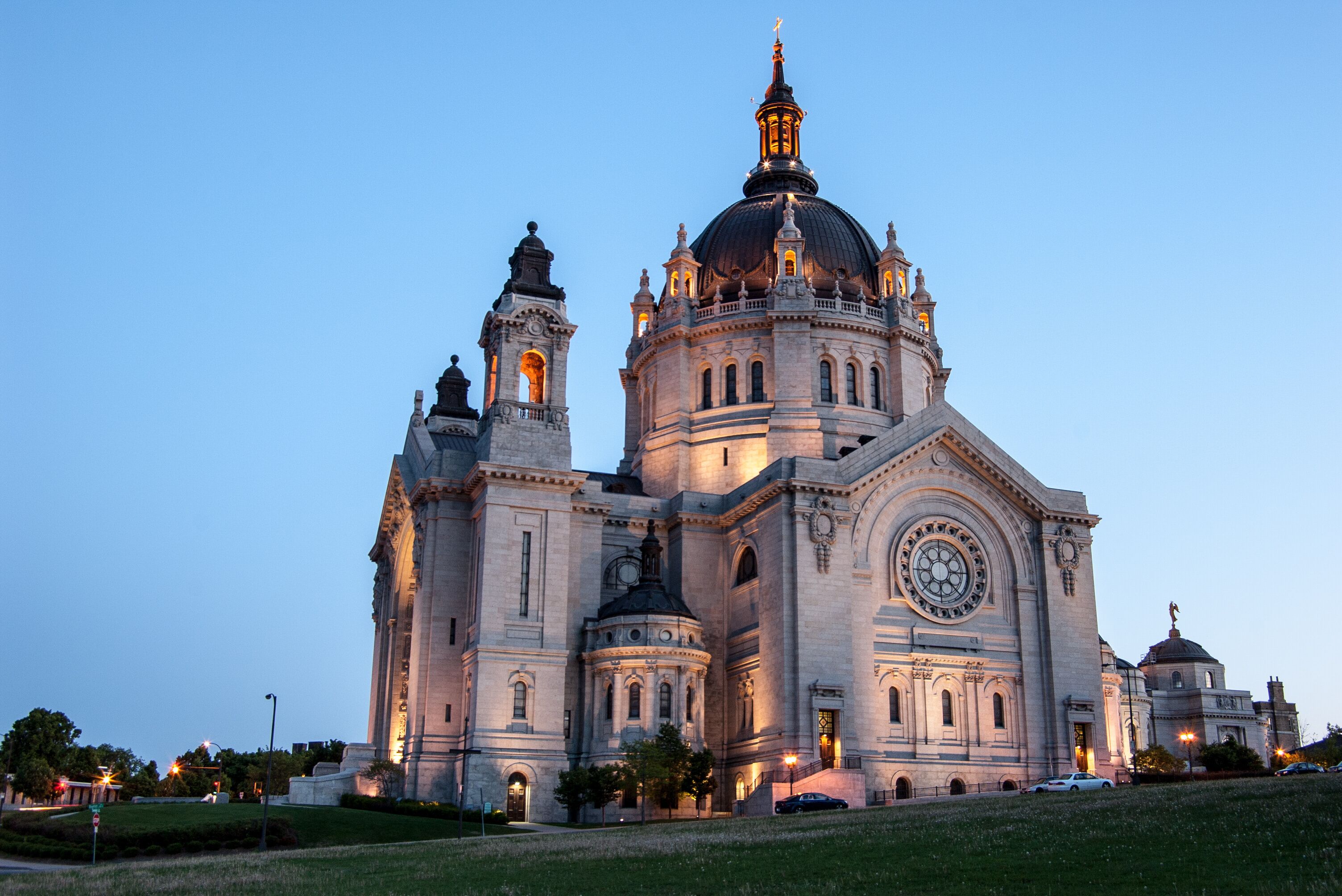 A large, historic cathedral with a prominent dome and twin towers, illuminated at dusk.