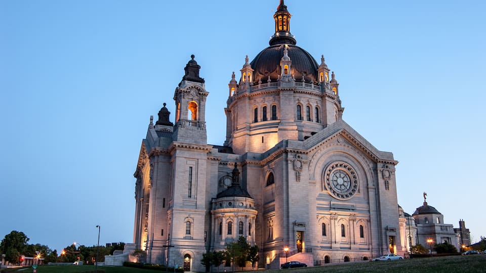 A large, historic cathedral with a prominent dome and twin towers, illuminated at dusk.