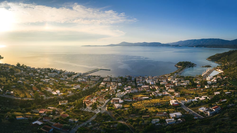 Vue aérienne d’une ville côtière dotée d’un port de plaisance, entourée de montagnes et bordée par une vaste étendue d’eau.