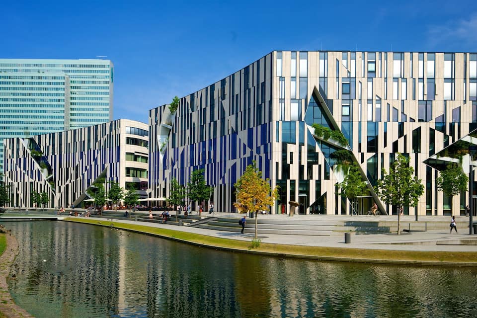 Ein modernes Gebäude mit vertikalen Linien und einem spiegelnden Wasserspiel davor.