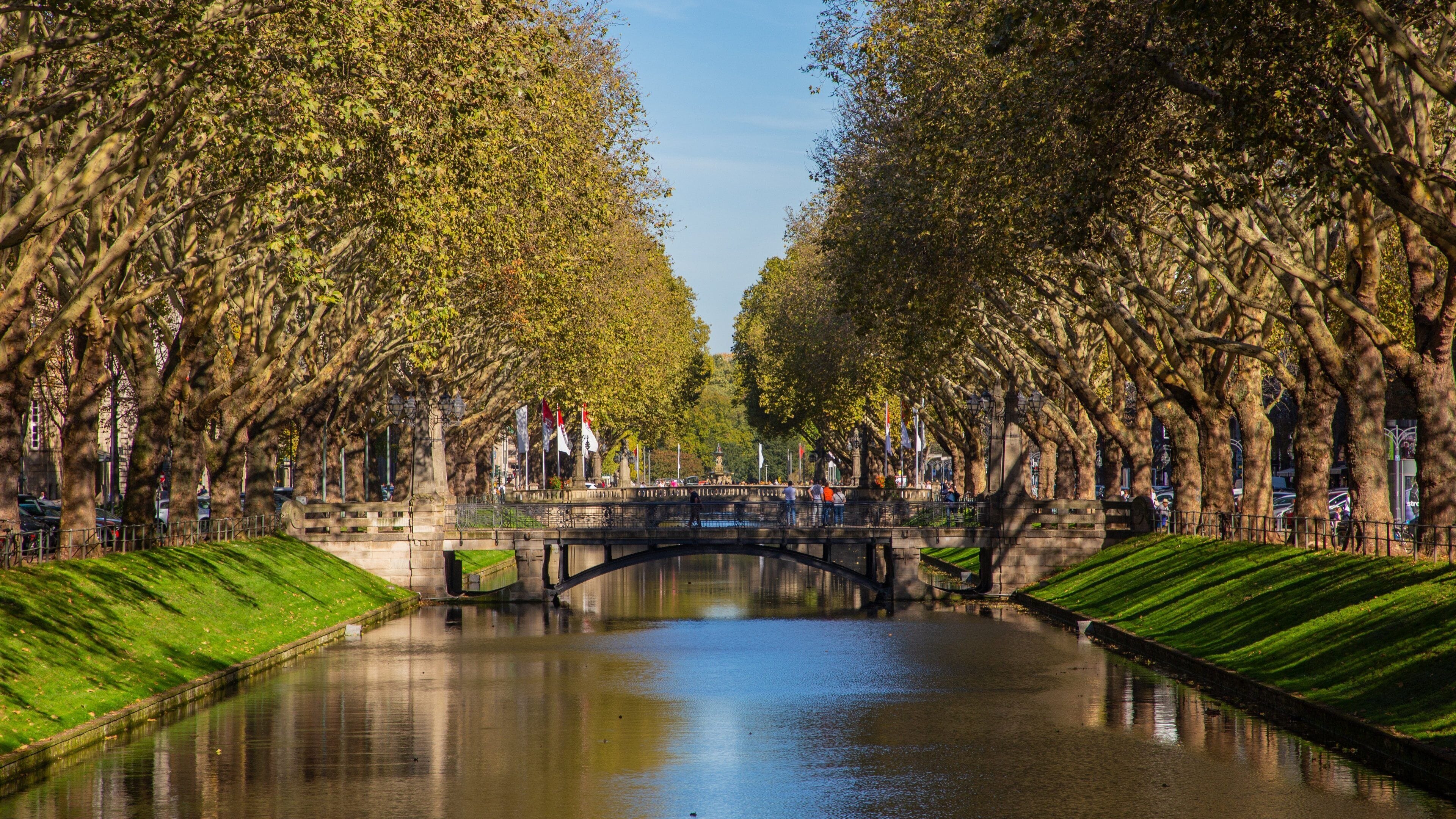 A canal flanked by trees, a stone bridge, and a statue.