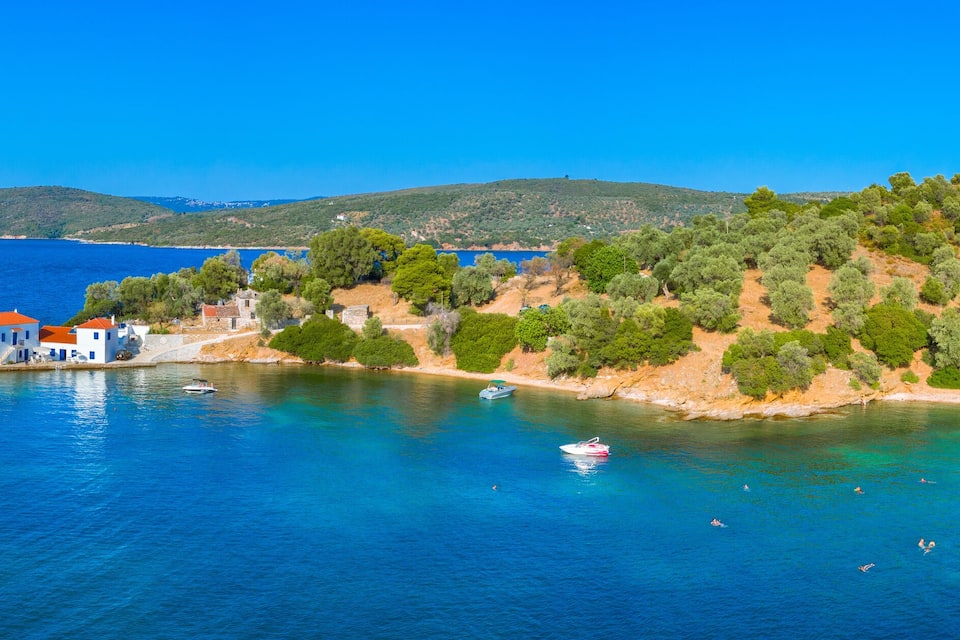 A coastal village with clear blue waters, boats, and a hilly backdrop.
