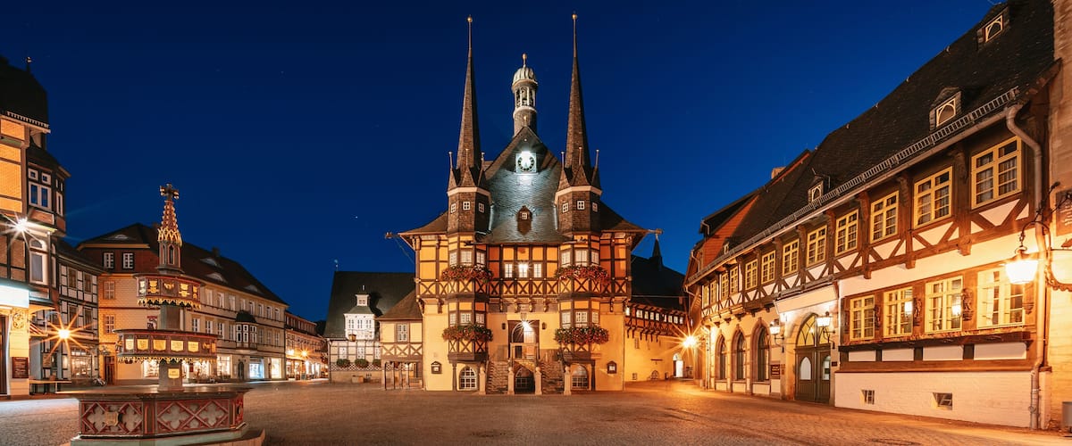 A historic town square with a prominent church featuring twin spires and a central fountain.