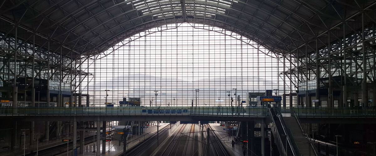 A large, modern train station with multiple tracks and a covered roof structure.