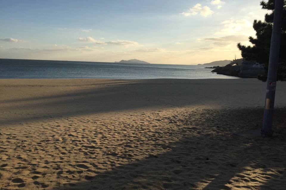 A beach with footprints leading to the water, a clear sky, and distant mountains.