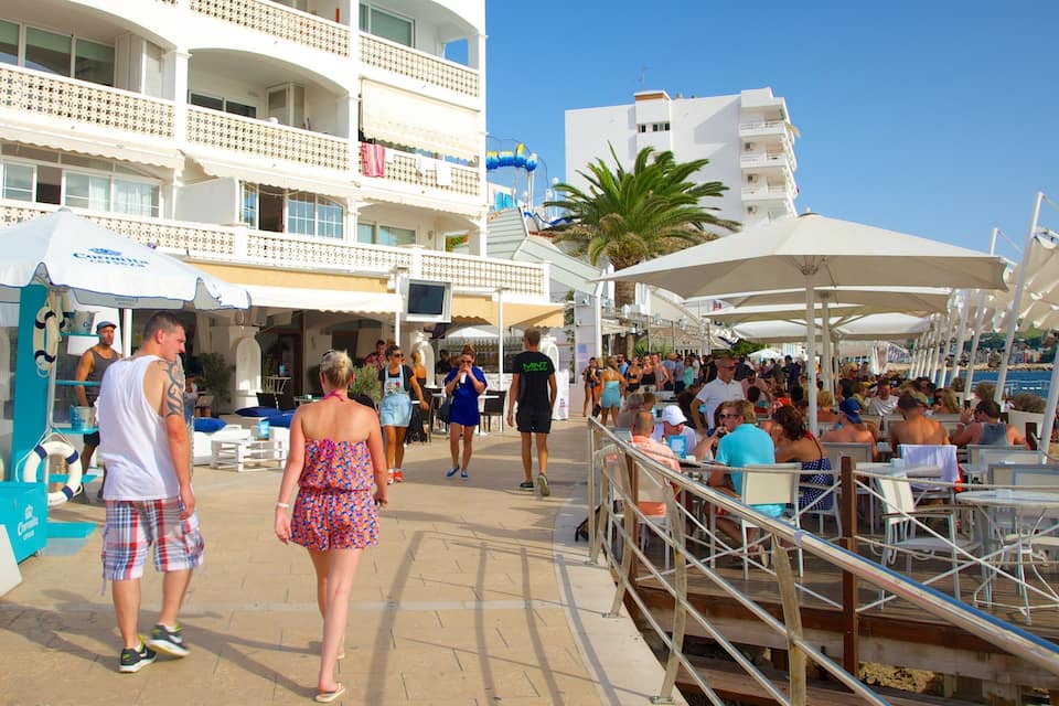 A crowded beachside promenade with people walking and sitting under umbrellas.