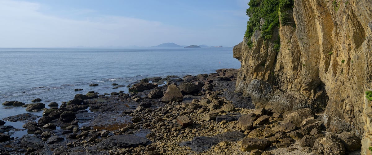 A rocky coastline with a steep cliff and a calm sea.