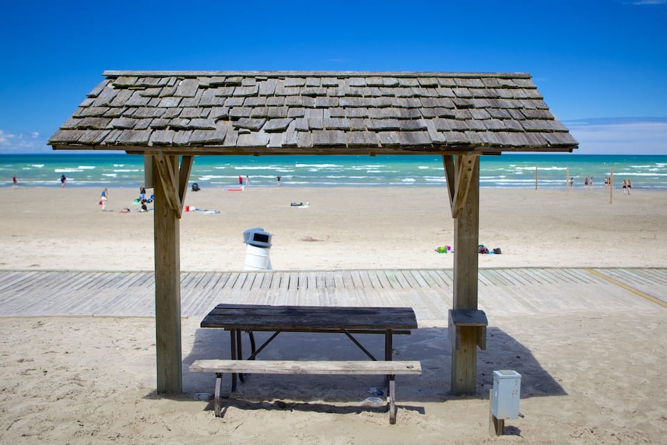 Un refugio de madera en la playa con un banco y un contenedor de basura.