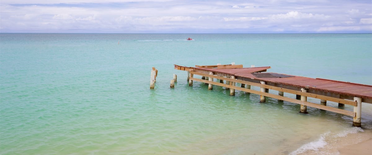 A wooden pier extending into turquoise water with a sandy beach at the end.