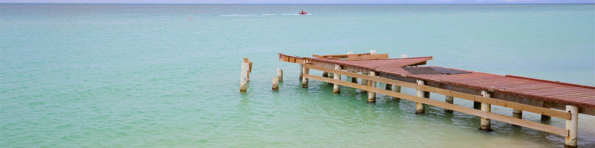 A wooden pier extending into turquoise water with a sandy beach at the end.