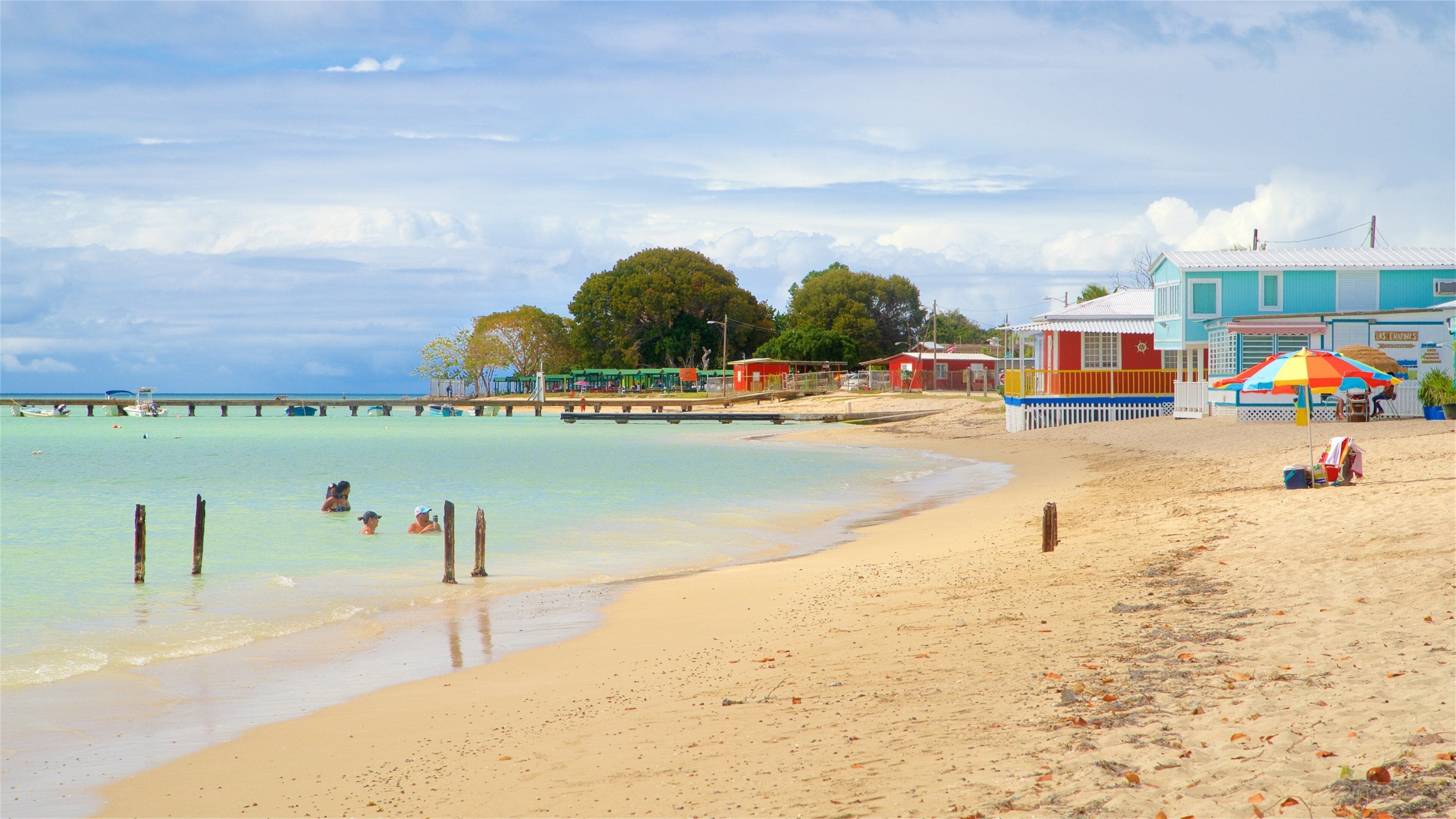 A beach with clear turquoise water, a sandy shore, and a pier with boats.
