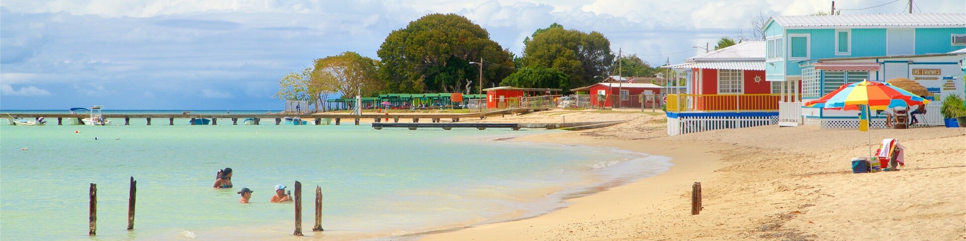 A beach with clear turquoise water, a sandy shore, and a pier with boats.